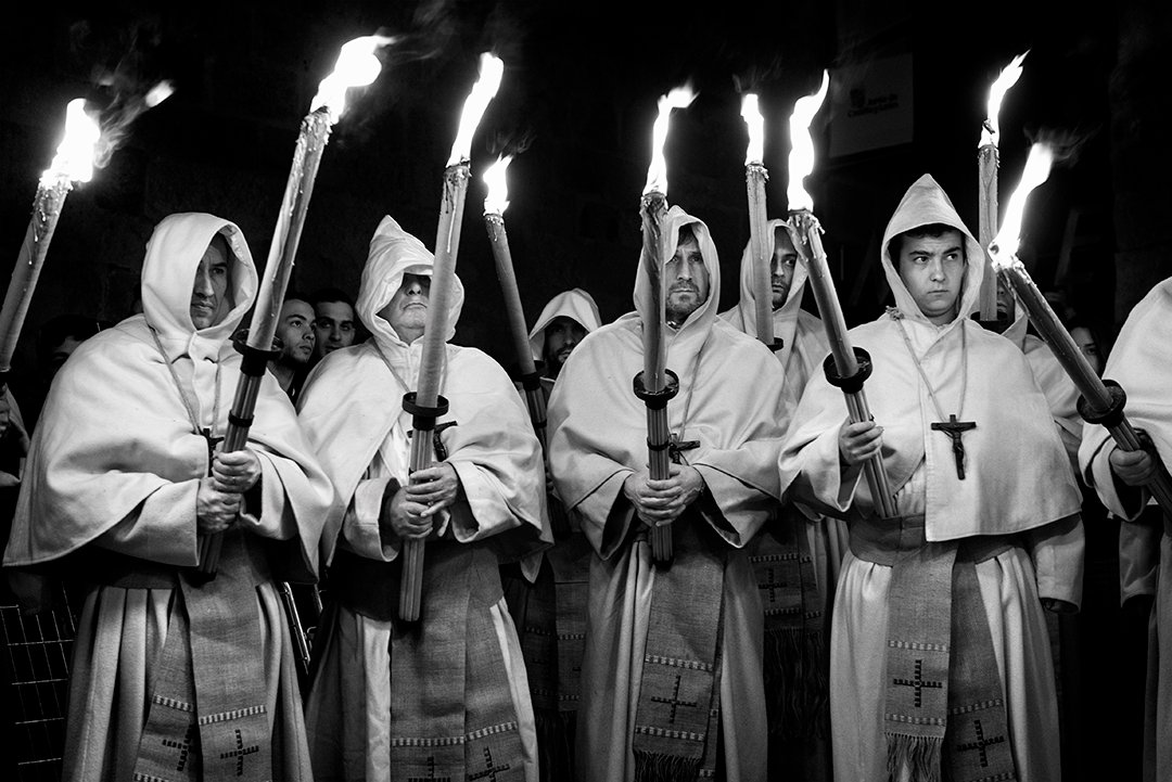 Personas con túnicas claras sostienen antorchas encendidas de noche.